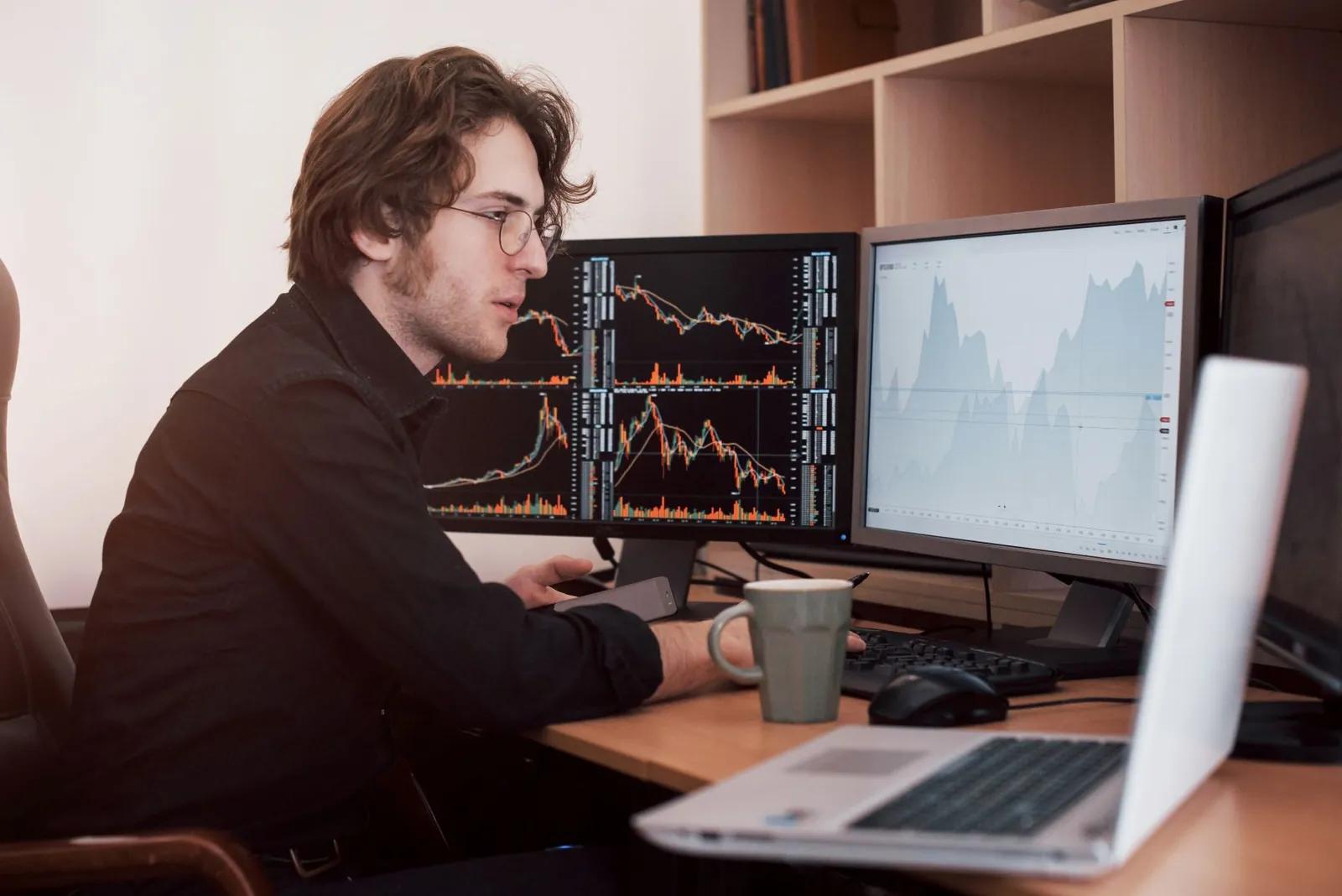 A trader at a desk reading charts across two monitors and a laptop.